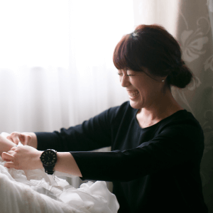 窓辺でドレスを整える女性ヘアメイクスタッフEikoのポートレート。