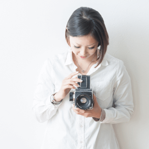 白シャツ姿でヴィンテージカメラを見つめる女性フォトグラファーAtsukoのポートレート。