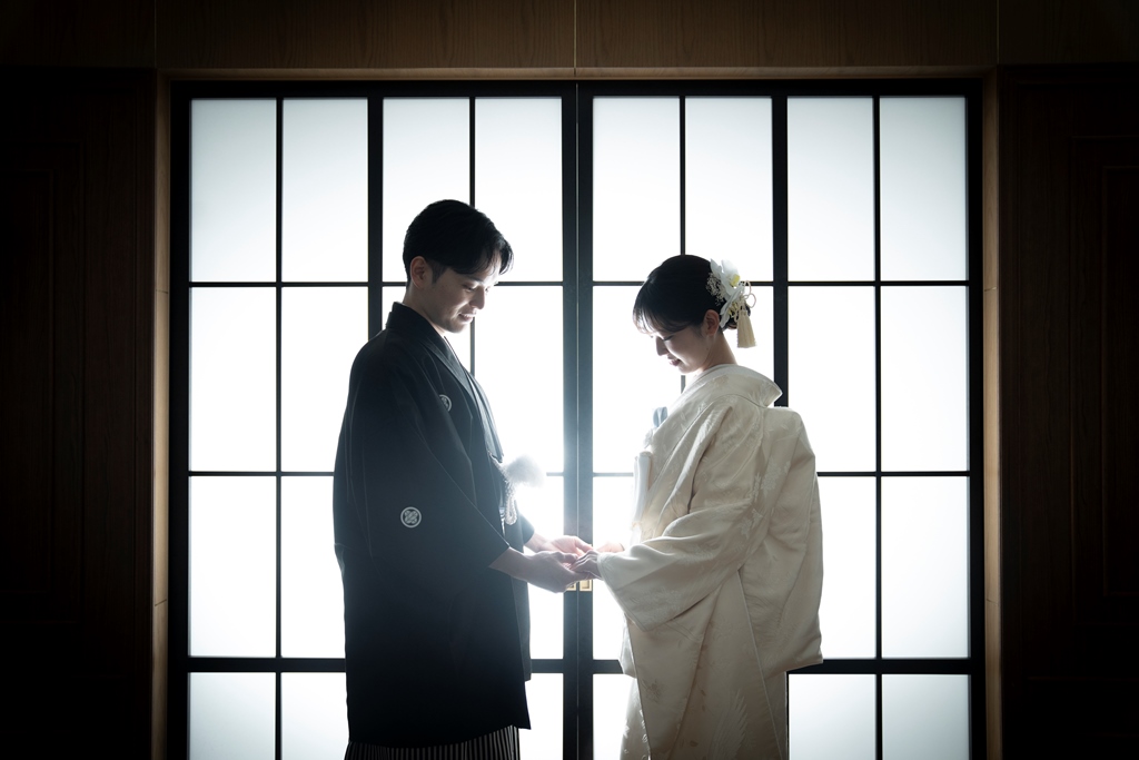 黒紋付袴姿の新郎と白無垢姿の新婦が障子窓の前で指輪を交換する、格子×ウッドの和モダンな空間にて
