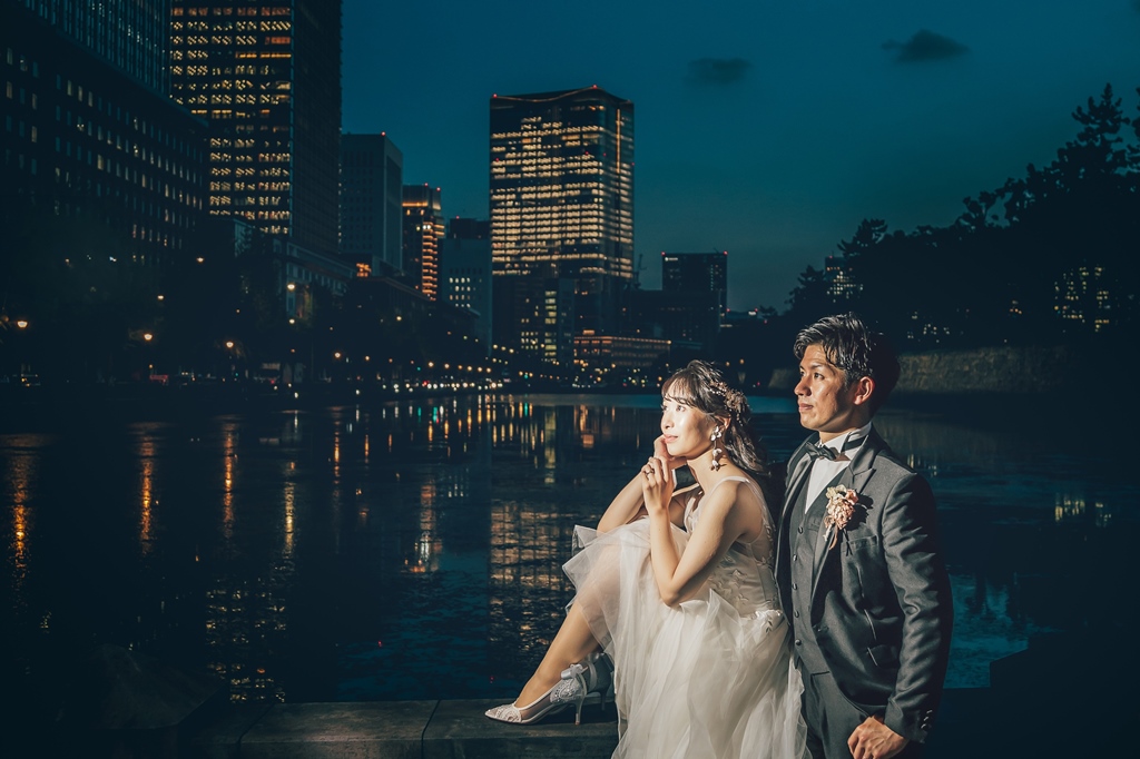 夜の内堀を背景に、頬に手を添え遠くを見つめる新婦と隣に立つ新郎。