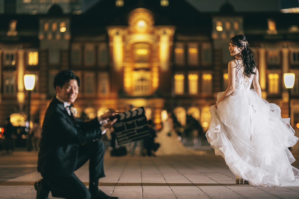 東京駅丸の内駅舎前でカチンコを持つ新郎、ドレスの裾を翻して振り返る新婦。