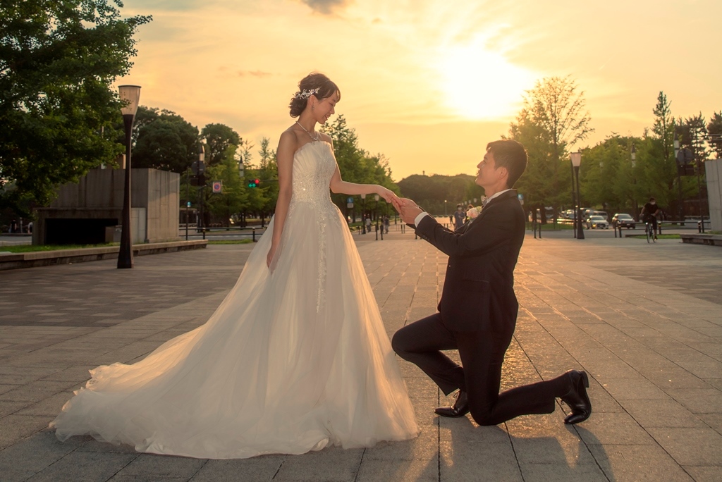 夕焼け空の下、片膝をつきプロポーズする新郎、驚いた表情で見つめる新婦。