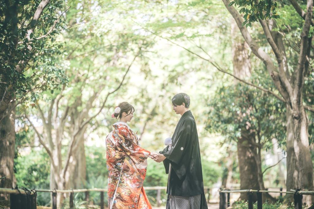 緑豊かな並木道で、朱色の色打掛の新婦と黒紋付の新郎が手を取り合い向き合う和装前撮り。