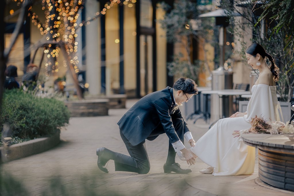 イルミネーションが灯るテラス席で、片膝をつき新婦の靴を履かせる新郎の可愛いポーズ。