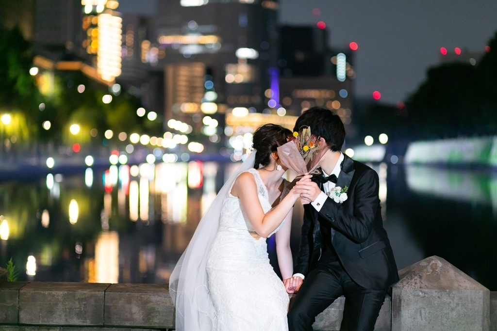夜の内堀端でブーケ越しにキスをする新郎新婦。