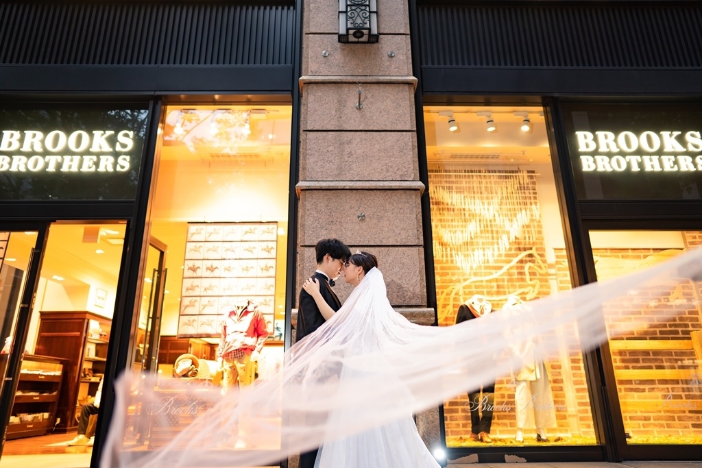BROOKS BROTHERSの店舗前でヴェールをなびかせながら寄り添う新郎新婦、ブリックスクエアらしいオシャレな街並みで。