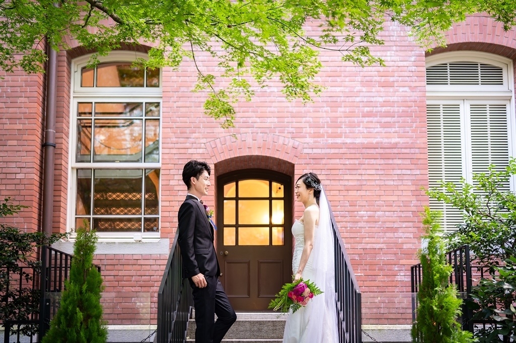 緑の葉が垂れる三菱美術館の扉の前で、見つめ合う新郎新婦。