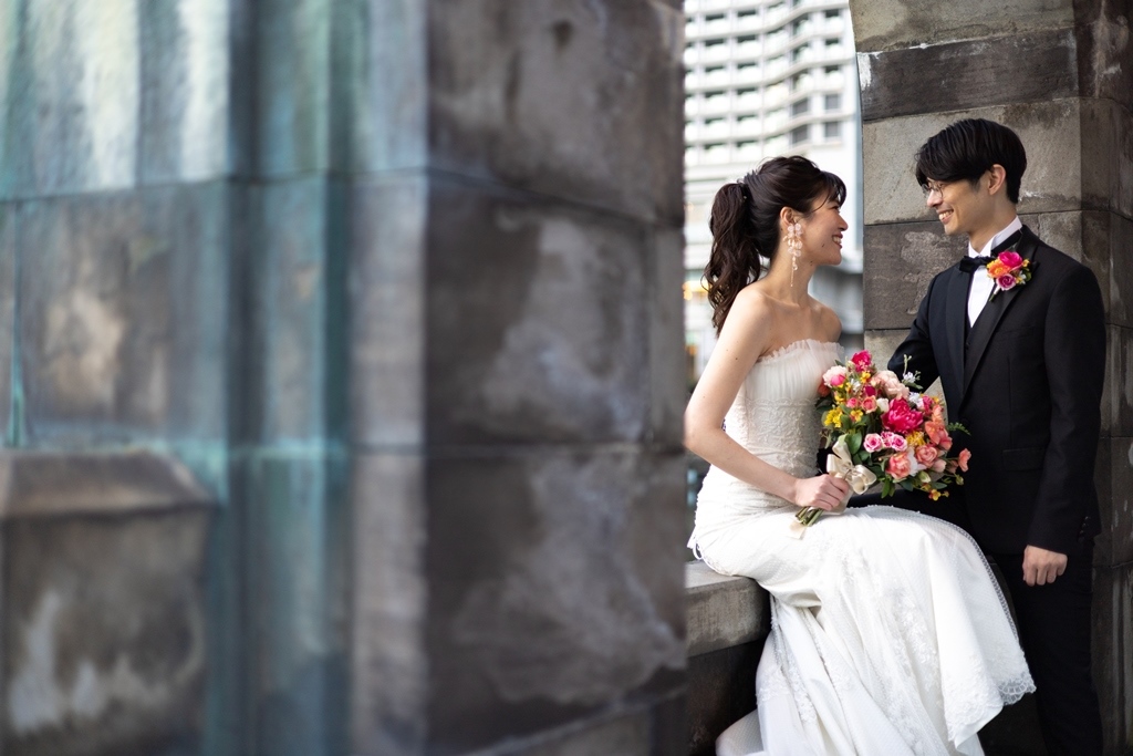 石柱の間で、色とりどりのブーケを手に見つめ合う新郎新婦。