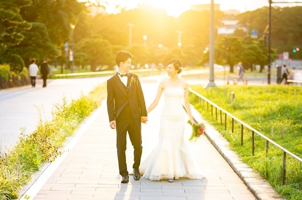 夕日に照らされた並木道を手をつなぎ歩く新郎新婦、新婦は白いマーメイドラインのドレス。