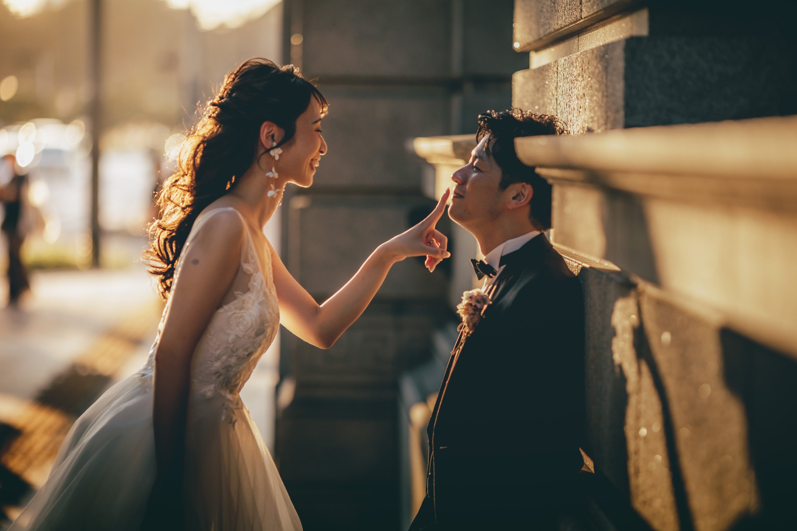 夕陽の逆光の中、新婦が指先を新郎の唇にそっと添える可愛らしいポーズの結婚写真。