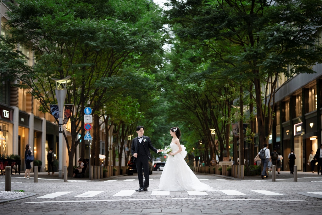 緑のトンネルのような並木道の横断歩道を、手をつないで渡る新郎新婦。