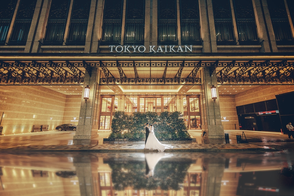 「東京會舘」の看板が輝く夜のエントランス前、水面に反射しながら寄り添う新郎新婦。