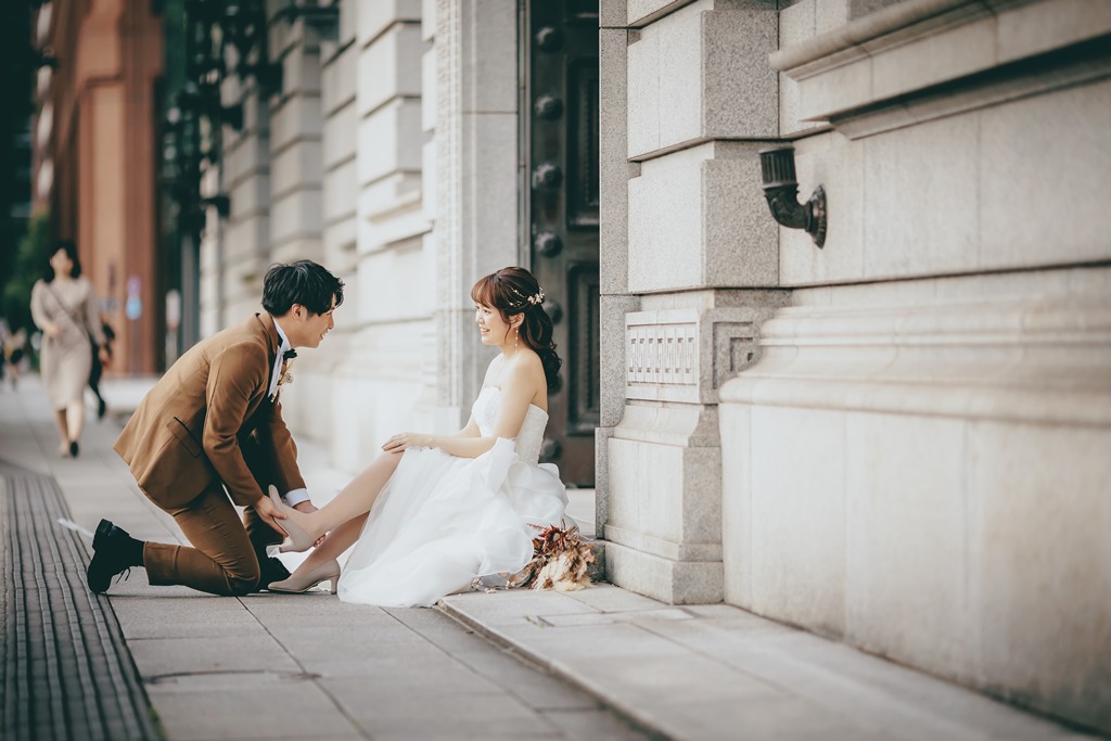 建物の入口で片膝をつき新婦の靴を直す新郎、ドライブーケが足元に置かれている。