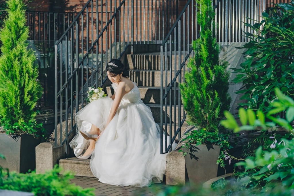三菱美術館の階段で片足の靴を直す新婦、ブーケを手に。