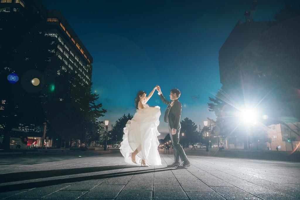 夜、輝く街灯を背景に手を取り合いダンスをする新郎新婦。