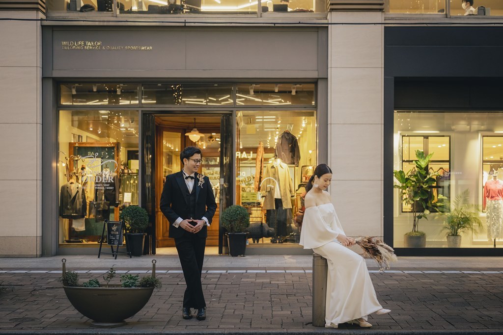 ブリックスクエアの店舗前、円柱に腰掛けドライブーケを持つ新婦を見つめる新郎。