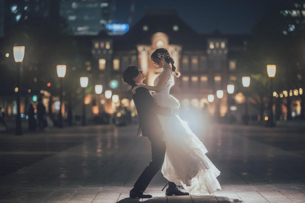 東京駅舎の夜景を背景に、新婦を高く抱き上げてダンスするように舞う新郎新婦。
