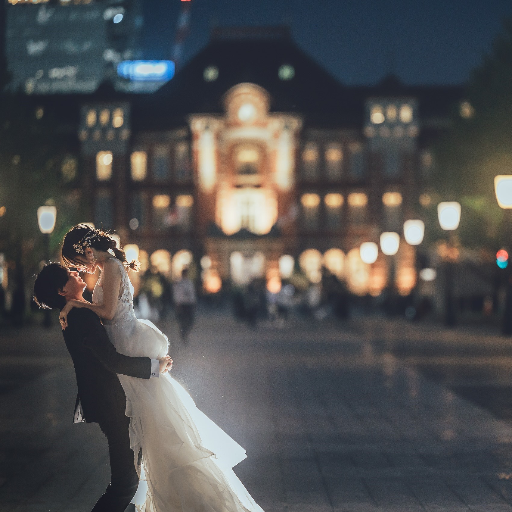 東京駅前の夜景を背景に、新婦を抱き上げる新郎の洋装ロケーションフォト。