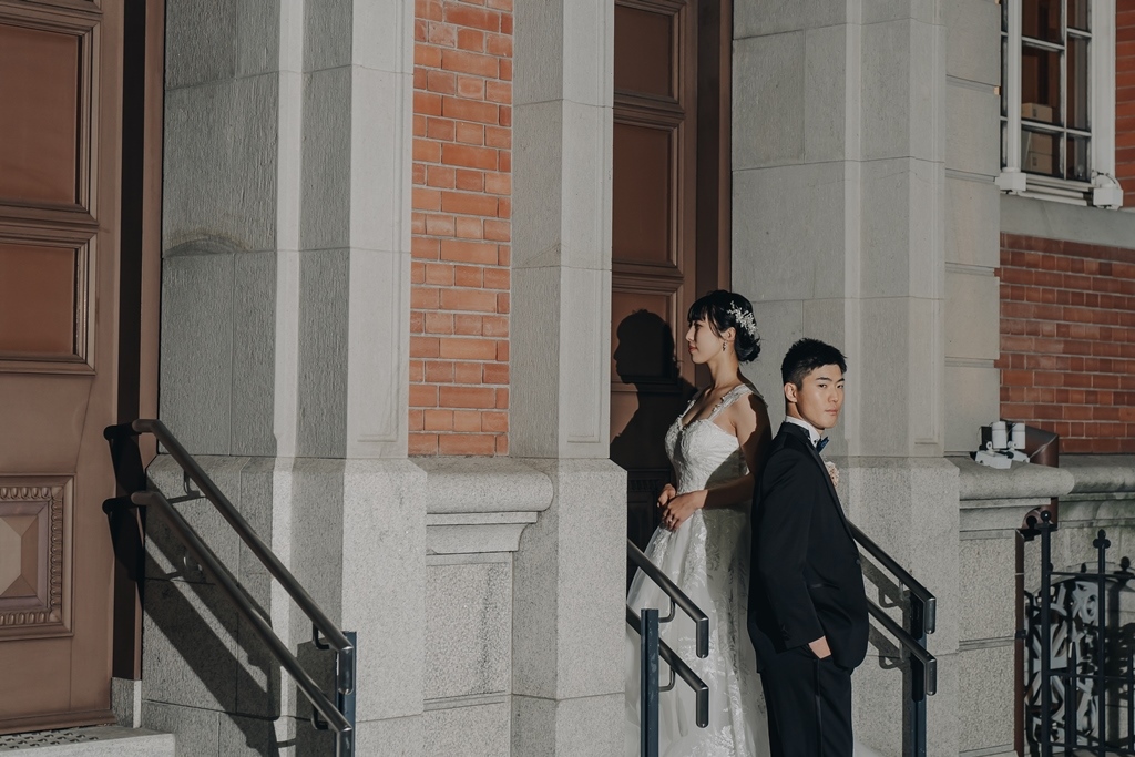 レンガと石造りの柱の前で、背中合わせに立つ新郎新婦。