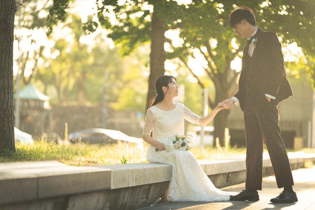 夕暮れの並木道の石段、腰掛ける新婦の手を取る新郎。
