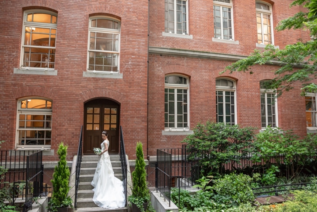 階段を上りブーケを持って佇む新婦、赤レンガの建物を背景に。