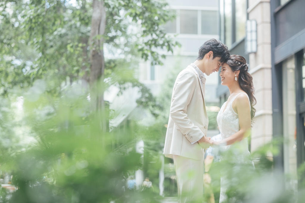 緑の街路樹を背景に、額を寄せ合う新郎新婦。
