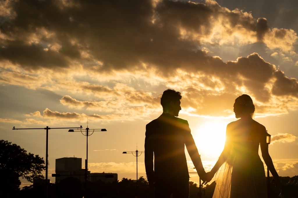 壮大な夕焼け空の下、雲間の光を背に手をつなぐ新郎新婦のシルエット。