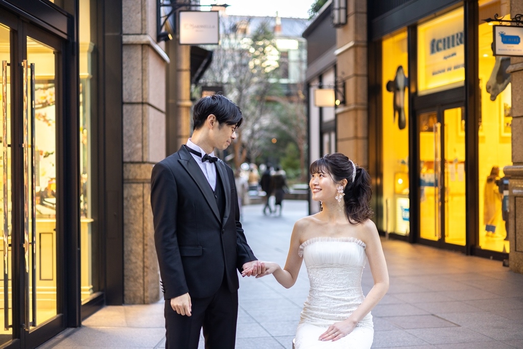 高級ブランド店が並ぶ並木道で見つめ合い手をつなぐ新郎新婦。