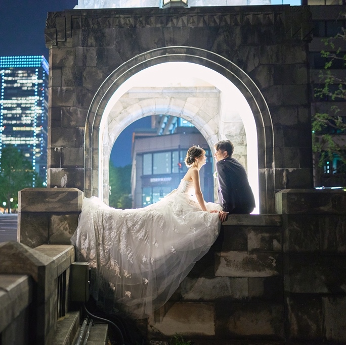 夜の東京駅を背景に、片膝をついてプロポーズする新郎と水面に映るリフレクションフォト。