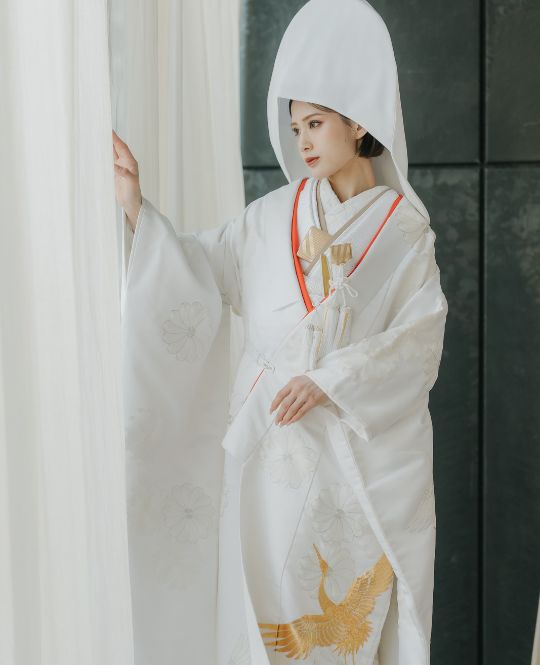 純白の白無垢に、白とゴールドの糸でほどこされた繊細な刺繍が上質な輝きを放ちます。さらに、他にはない赤いラインを配し伝統の中に凛とした個性を添えた、格調高い一着です。花嫁の清らかさと格式を美しく引き立て、特別な一日を永遠の記憶へと昇華させます。白無垢の中でも写真映えも格別です。和の美を体現する一着。