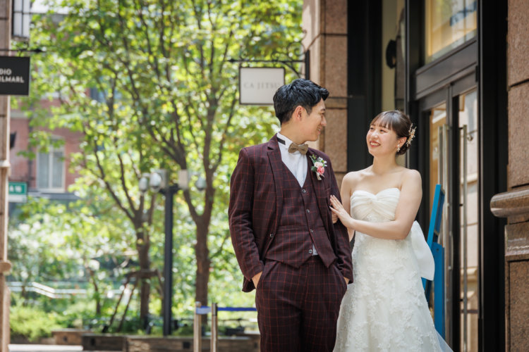 東京駅を背景に、ウェディングドレスとタキシード姿で並ぶおふたりの爽やかな昼間のウェディングフォト