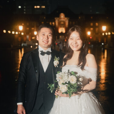 東京駅丸の内駅舎のライトアップを背に、白バラのブーケを持って並ぶ新郎新婦。雨の夜に撮影したフォトウェディング