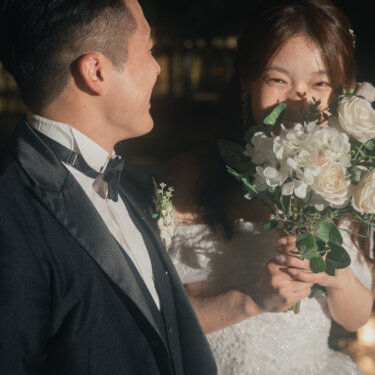白バラのブーケで口元を隠して笑う新婦と、つられて笑い出す新郎。自然な表情を捉えた前撮りのスナップ
