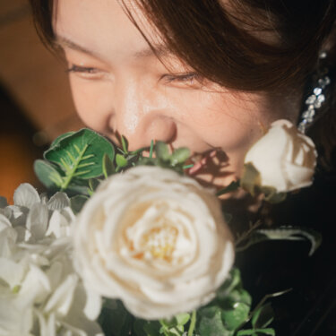 白バラのブーケに顔をうずめて笑う新婦のクローズアップ。やわらかな光に包まれたフォトウェディングの一枚