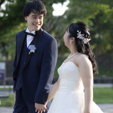 新緑の木立を背に手をつなぎ、見上げて笑う花嫁と新郎。自然光あふれる東京駅周辺のロケーションフォト