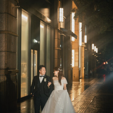 街灯が連なる雨上がりの丸の内仲通りを歩く新郎新婦。濡れた石畳に光が反射する東京駅すぐの夜の前撮り