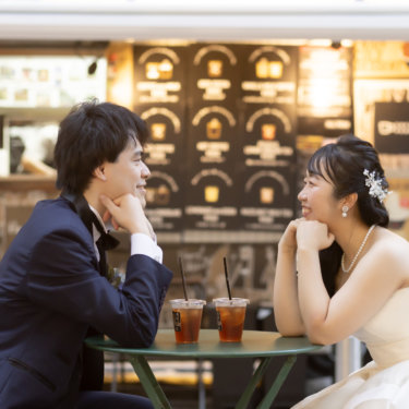 カフェテーブルで頬杖をつき語り合う新郎新婦。丸の内仲通りのキッチンカーを背にした街ロケ前撮り