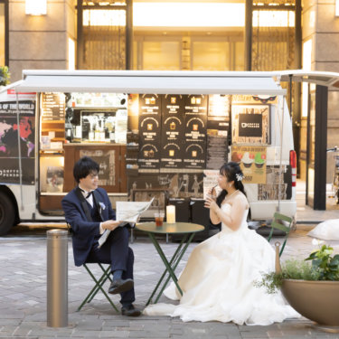 キッチンカーの前のカフェテーブルでくつろぐ新郎新婦。丸の内仲通りの日常に溶け込んだロケーション前撮り