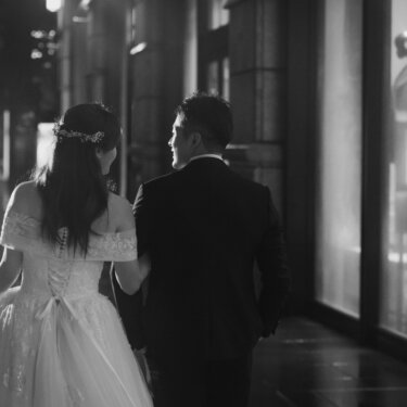 ショーウィンドウが並ぶ丸の内仲通りを腕を組んで歩く新郎新婦の後ろ姿。ドレスの裾を持ち上げたモノクロの一枚