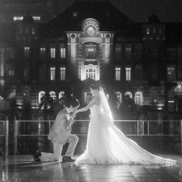 モノクロで表現した、ひざまずいて手を取る新郎と長いトレーンの新婦。雨の東京駅前広場でのフォトウェディング