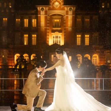 片膝をついて新婦の手を取る新郎。東京駅丸の内駅舎のライトアップとロングベールが美しい夜の結婚写真