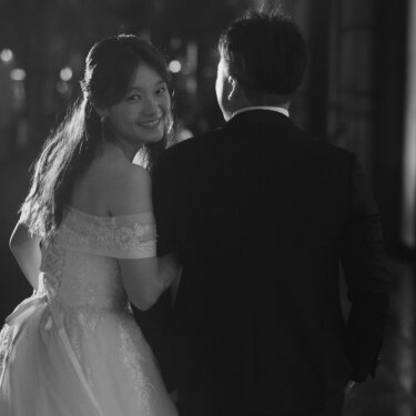 夜道を歩きながら振り返って微笑む新婦と、寄り添う新郎の後ろ姿。街灯がにじむモノクロのフォトウェディング