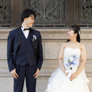 装飾的な鉄扉を背に、階段へ腰かける花嫁と立つ新郎。歴史ある建物の前で撮る結婚写真