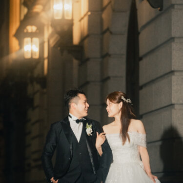 連なるガス灯風の外灯の下で微笑み合う新郎新婦。重厚な石造り建築が続く夜の丸の内でのロケーションフォト