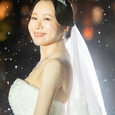 雨粒が舞う夜、ティアラとロングベールをまとった新婦の横顔。背景は東京駅丸の内駅舎のライトアップ。東京駅の夜のフォトウェディング