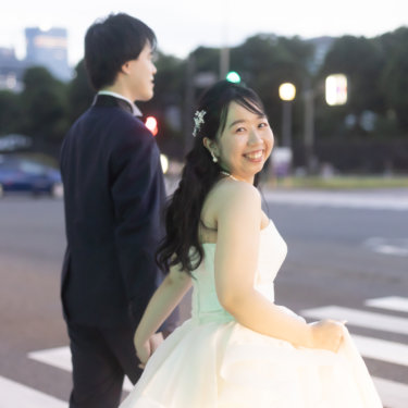 横断歩道の途中で振り返り、ドレスの裾を持って微笑む花嫁。夕暮れの街で撮るウェディングフォト