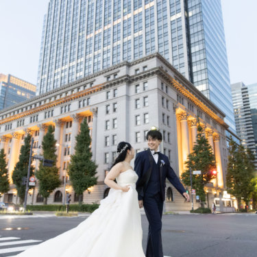 ライトアップされた石造建築と高層ビルを背景に、横断歩道で笑い合う新郎新婦。丸の内の街ロケフォトウェディング