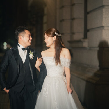 石造りの洋館の壁を背に腕を組んで歩く新郎新婦。夜の丸の内で撮るフォトウェディング