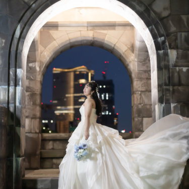 石造りの二重アーチの中でドレスの裾を大きくなびかせる花嫁。ビルの灯りを背にした東京駅周辺のナイトフォト