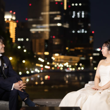 石積みのアーチの中で向かい合い、笑顔で語らう新郎新婦。丸の内の夜景が広がるナイトフォトウェディング